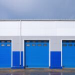 Trzy niebieskie bramy przemysłowe segmentowe z przeszkleniami w górnej części konstrukcji